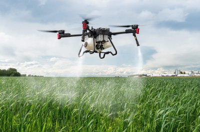 Agriculture drone against background of blue sky and green fields with agricultural plants. Quadrocopter for pollination of plants. Modern technologies in agriculture.
